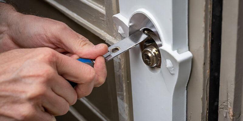 Close-up of hands using a chisel to adjust the size of the hole in a door to fit a new lock.