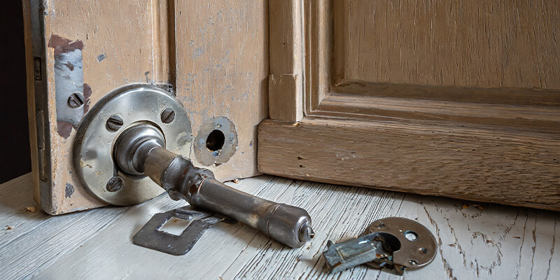 An old doorknob and latch removed from a door, with empty holes in the door where the hardware used to be.